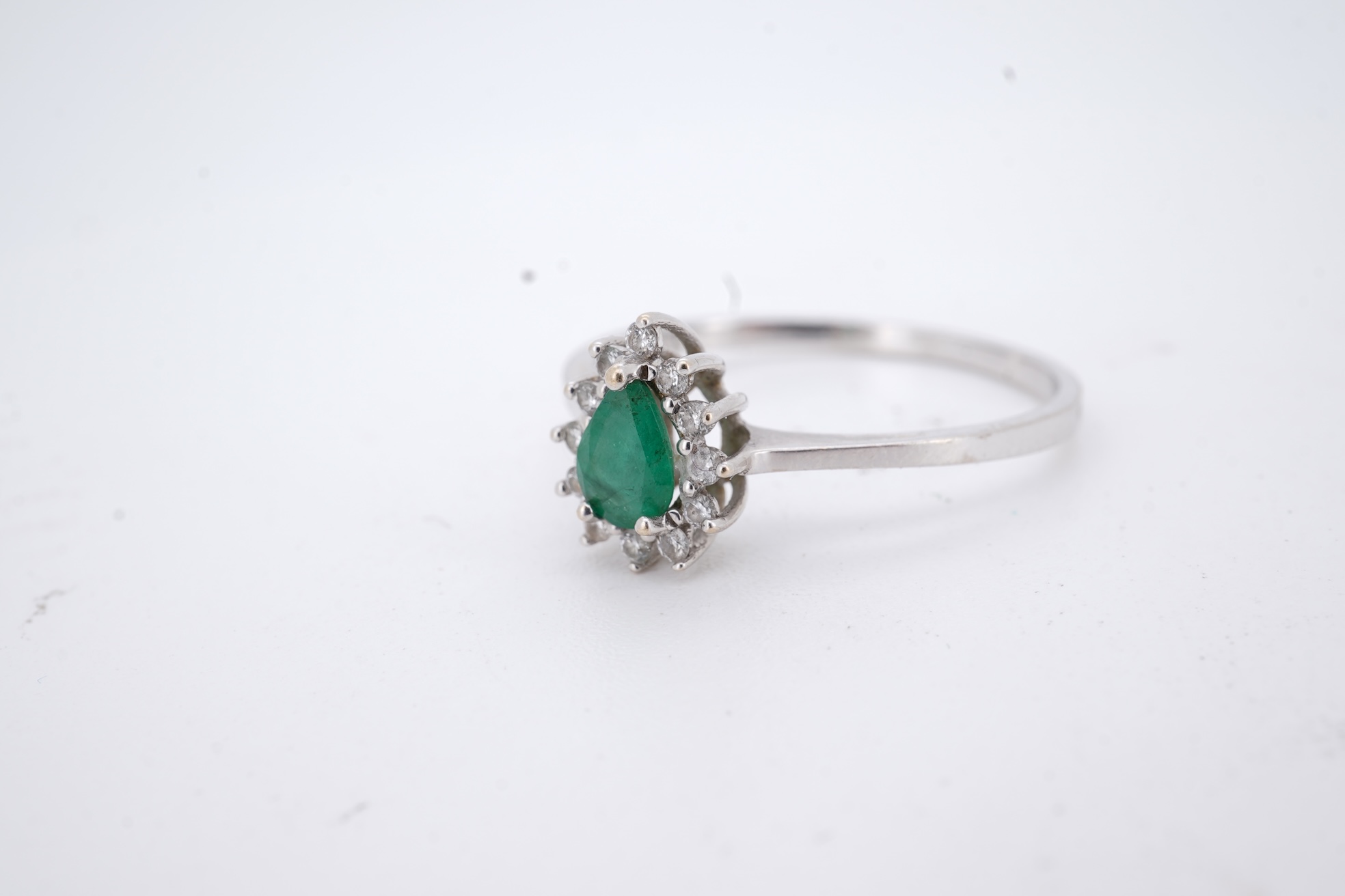 A modern white metal(stamped 14k), emerald and diamond set pear shaped cluster ring, size R, gross weight 1.3 grams.